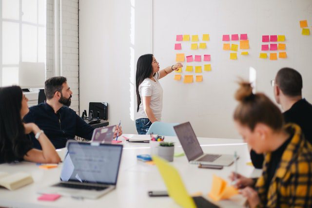 Woman addressing a meeting and placing sticky notes on the wall