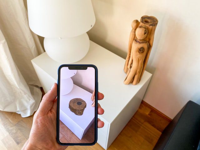 a hand using AR on a mobile phone to show a piece of wood on a table