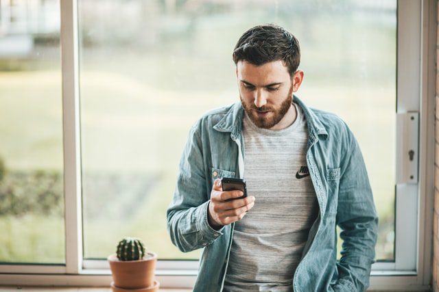 A man uses a cell phone while leaning on a window