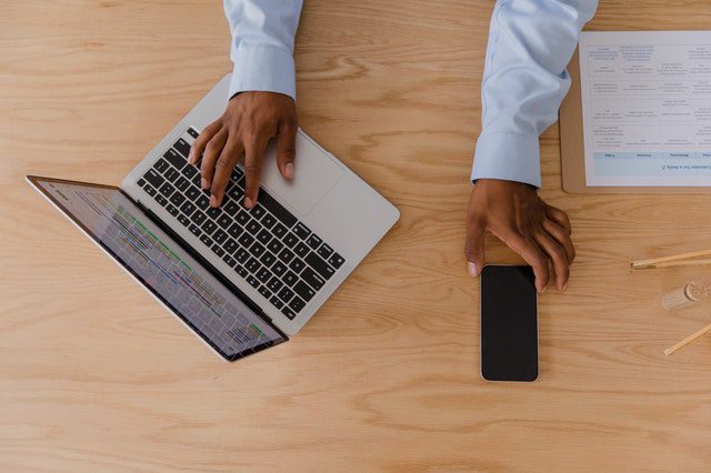 man's hands typing on a laptop and holding a mobile phone on top of a table