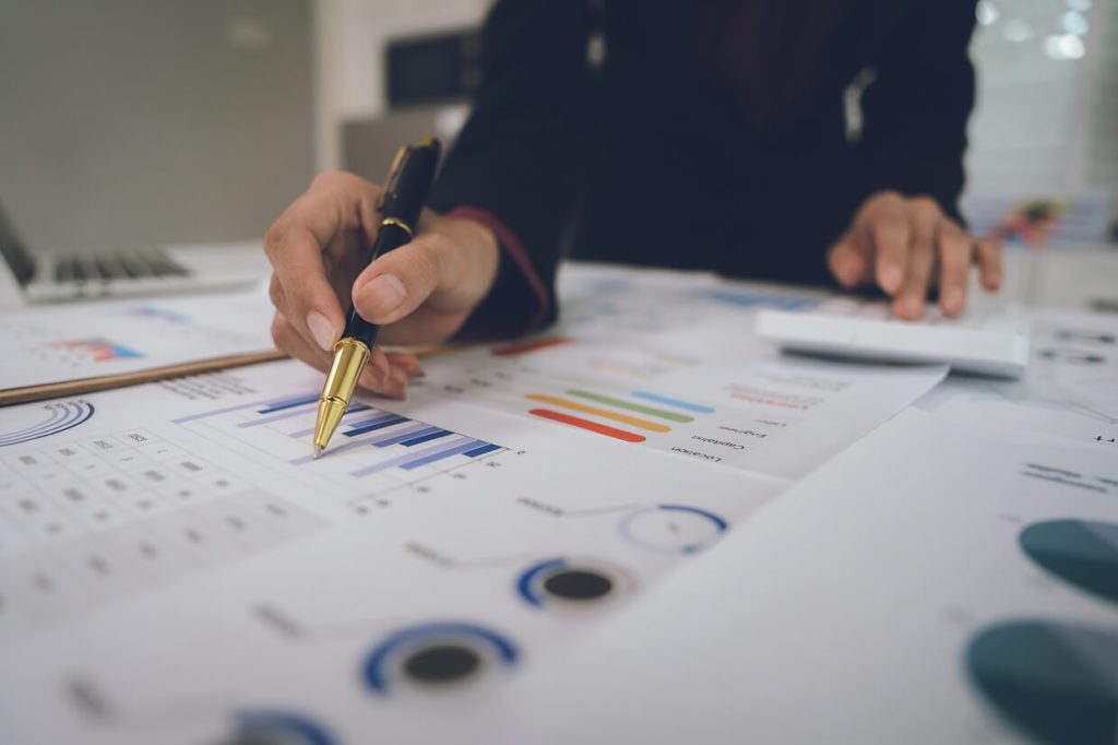 person holding a pen over graph printouts