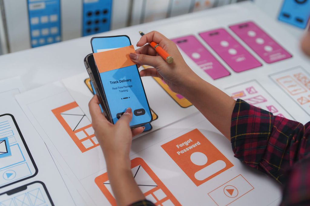 Hand holding a cell phone and a pen with labels on the desk
