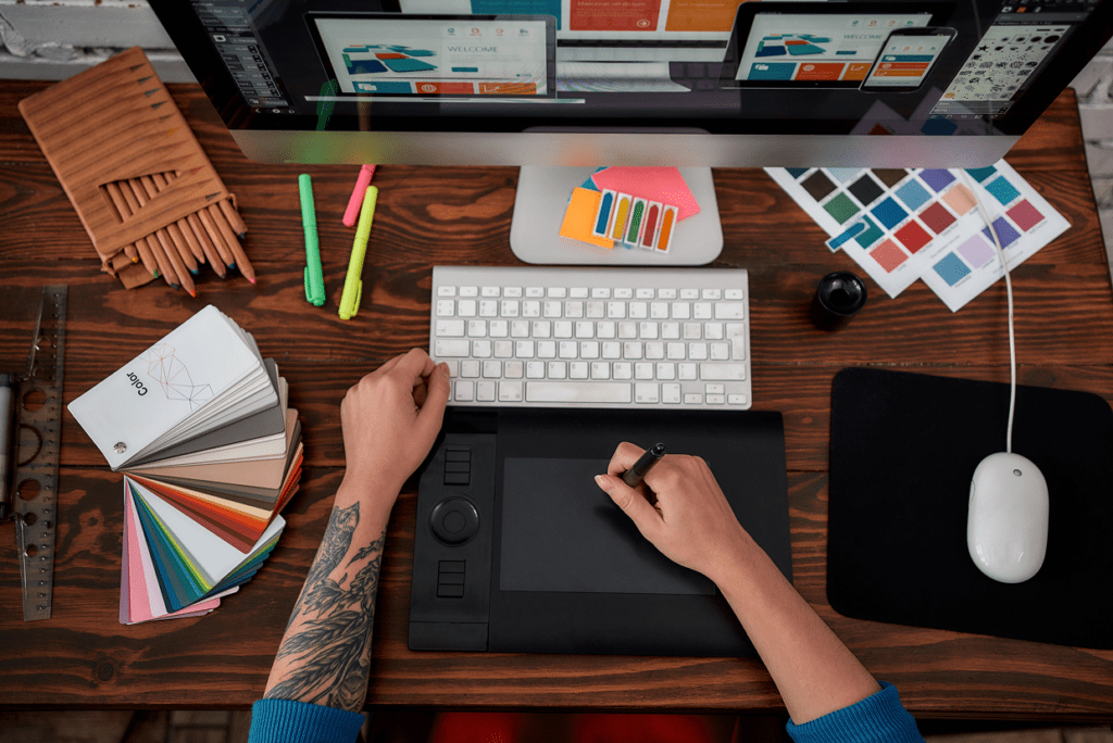 Desk with large monitor showing mockups, keyboard, highlighters, post it sheet, keypad
