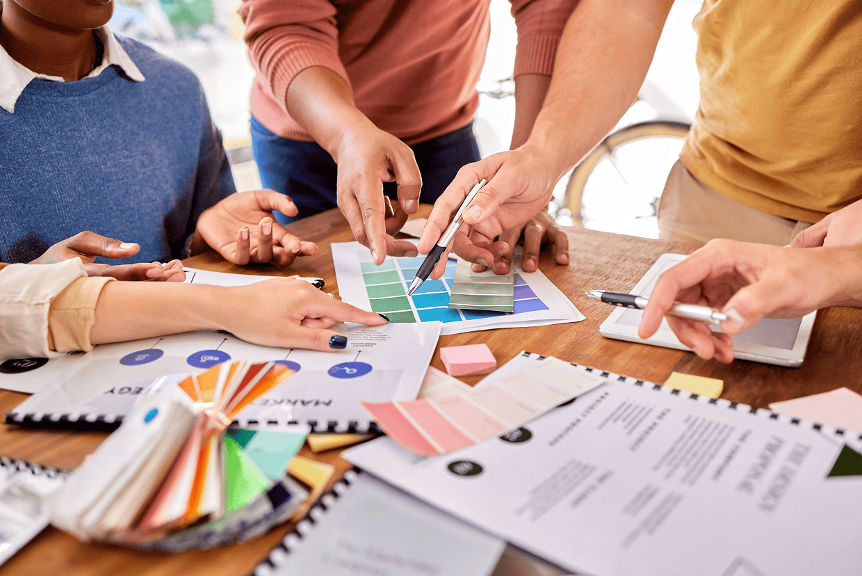 Multiple hands pointing to charts and post its on desk