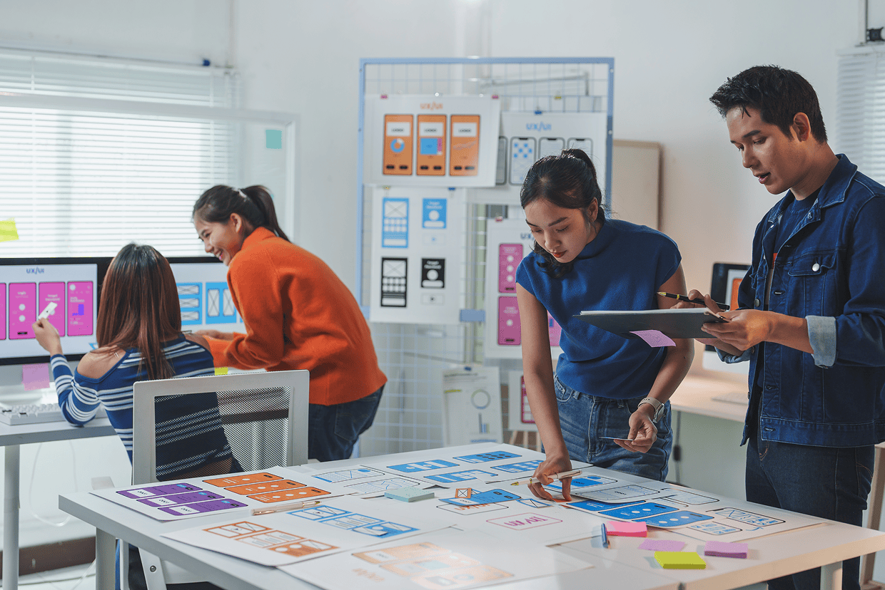 Image of a room with 4 individuals examining mockups on a screens and on paper