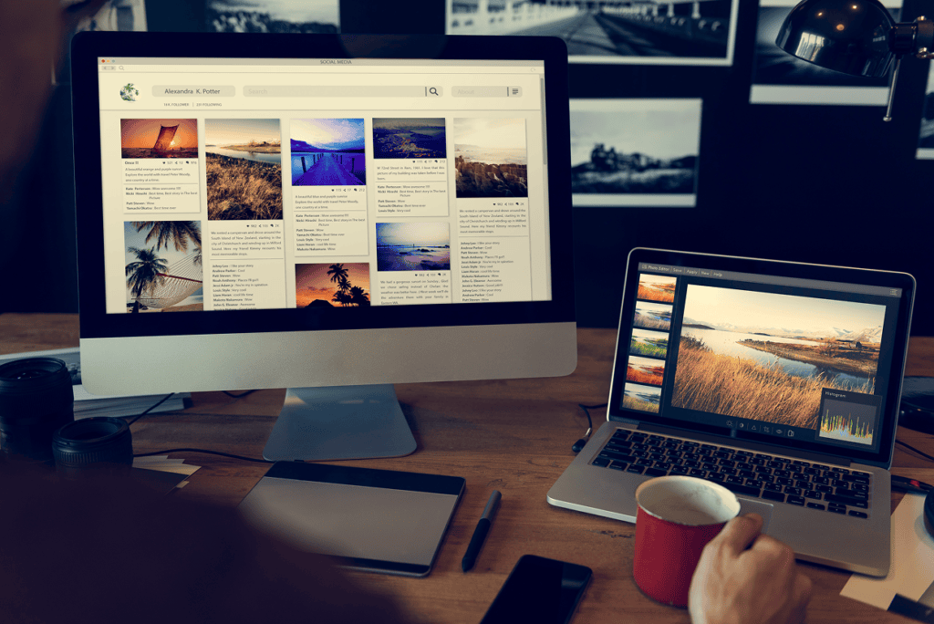 Multiple screens with images on a desk with someone seated holding a red cup