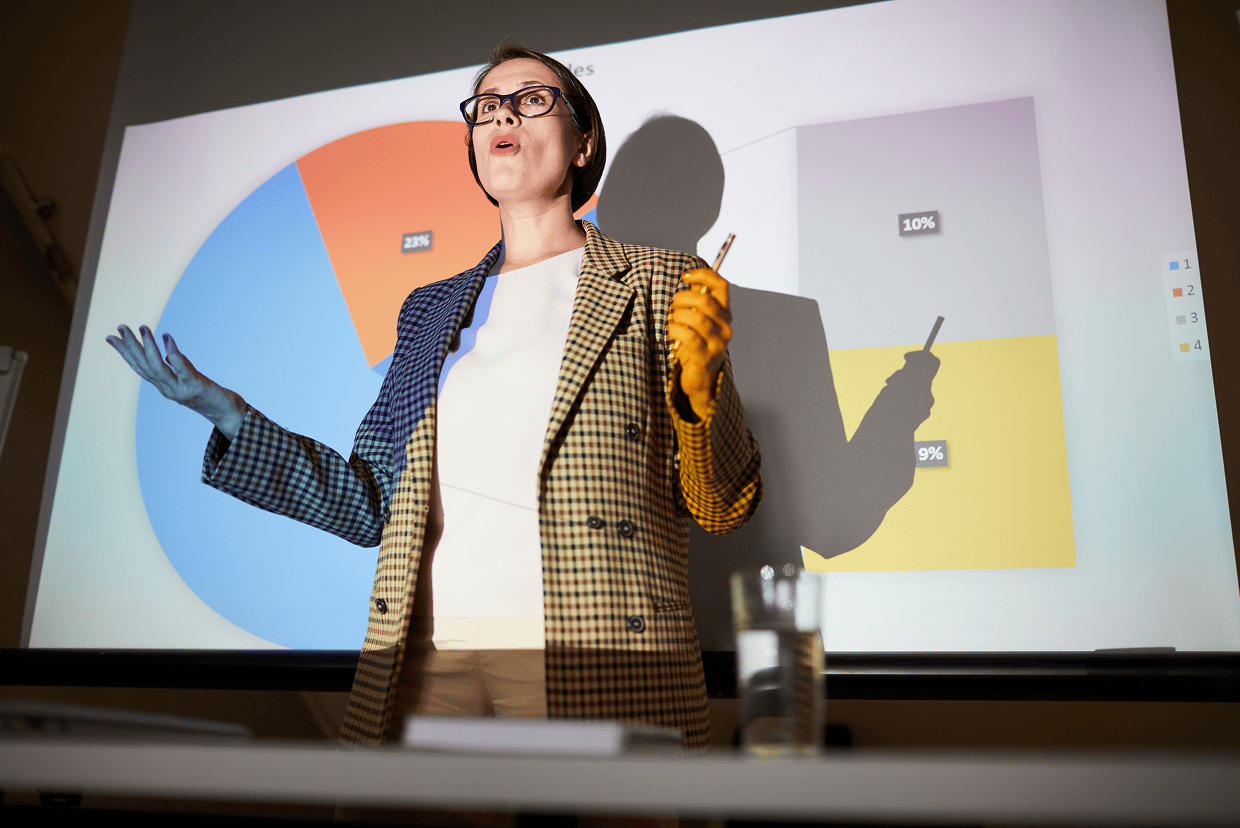 Woman in plaid jacket holding a pencil in front of white board with chart